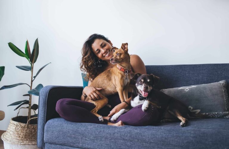 A woman sitting on a couch smiling while holding two small dogs in her lap.