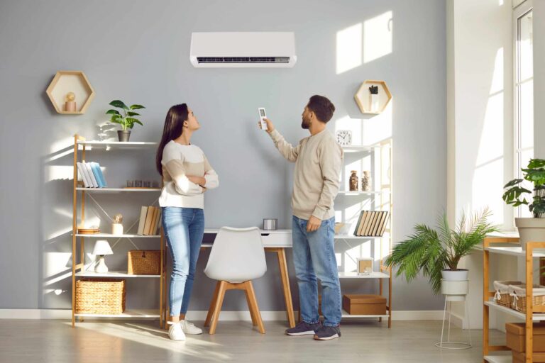 A young couple standing together in a living room, adjusting a wall-mounted air conditioner control panel.