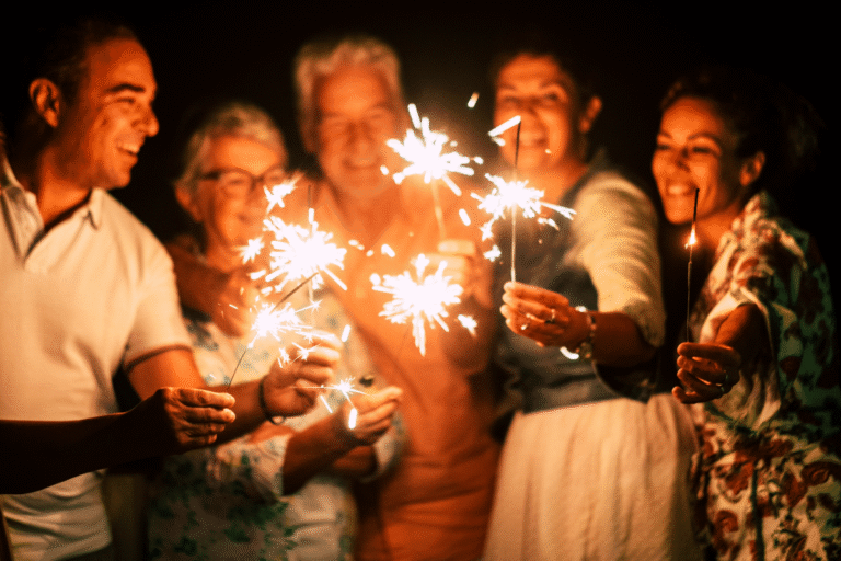 A group of adults smiling and holding lit sparklers together outdoors at night, celebrating New Year's.