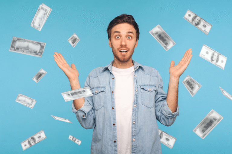 A surprised young man with hands raised as cash bills fall around him against a blue background.